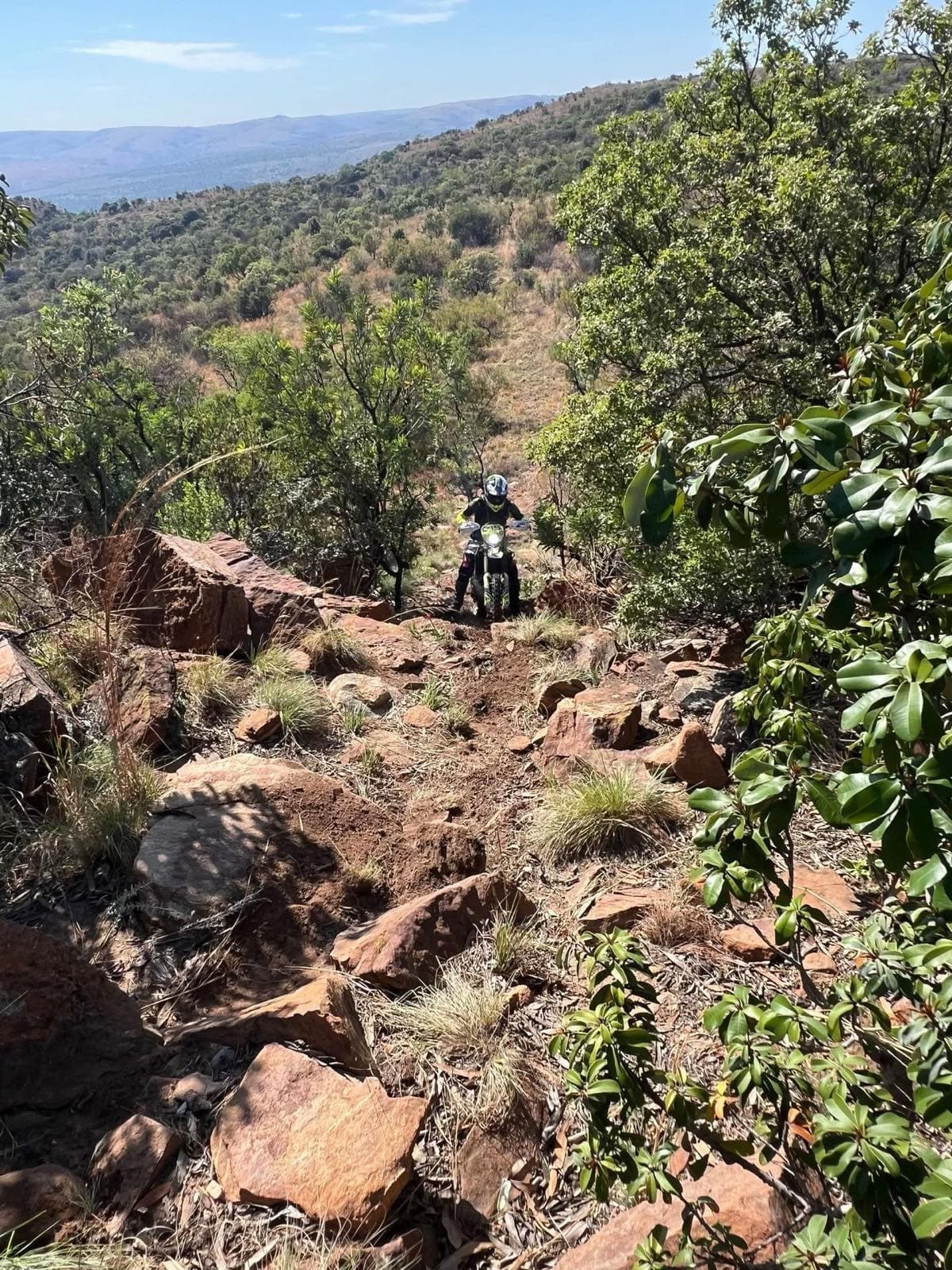 Rider on a steep rocky hillside with the valley behind